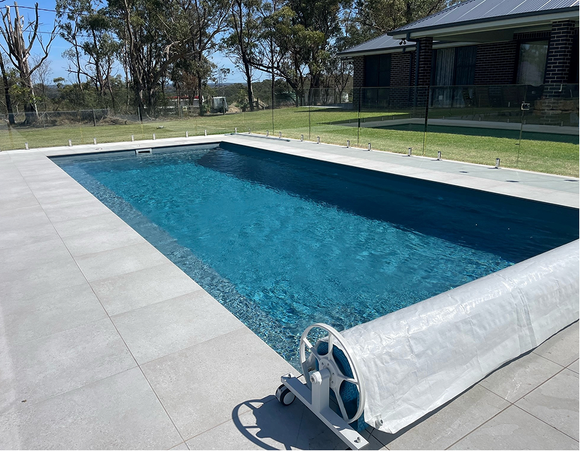 Modern in-ground backyard swimming pool with paved coping and glass pool fencing designed by LC Design & Drafting.
